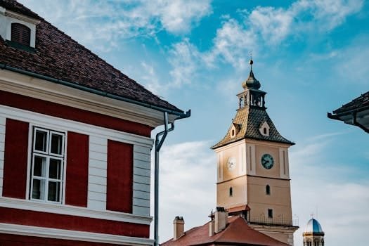 Charming historic clock tower with red rooftops in Brașov, Romania under a clear blue sky.